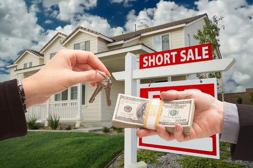 two hands exchanging keys to each other in front of a house