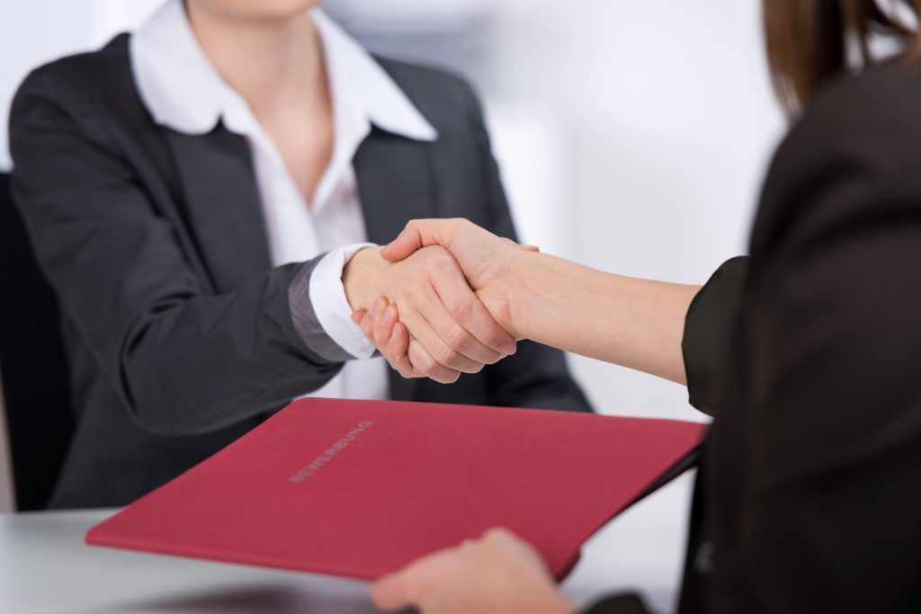 two women shaking hands over a red folder