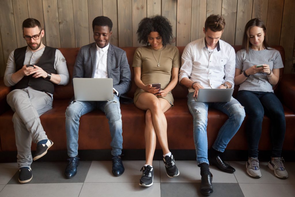 four people sitting on a couch using their laptops