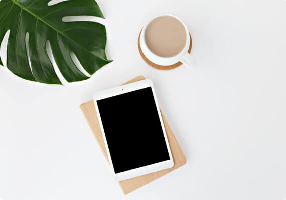 a tablet, coffee cup and plant on a white table