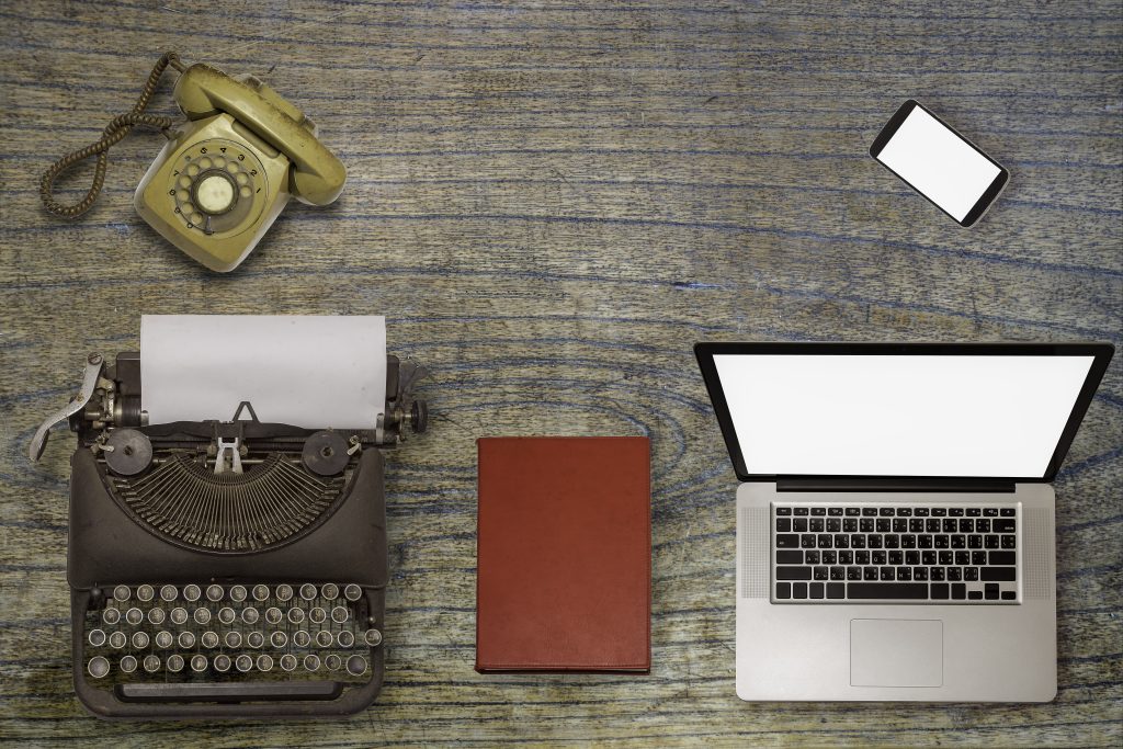 a desk with a laptop, phone and typewriter