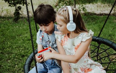 two children sitting on a swing playing with headphones