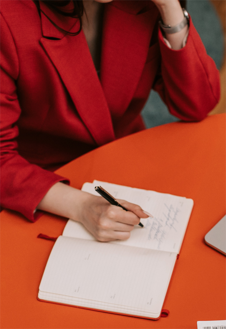 a woman in a red jacket writing on a notebook