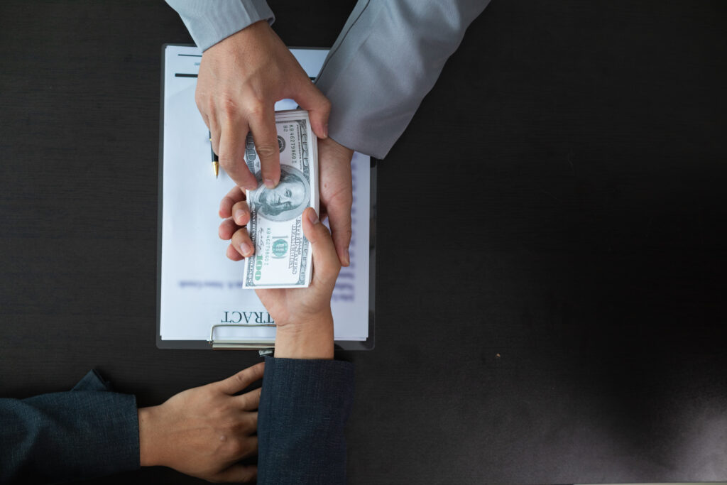 two people are exchanging money in front of a laptop